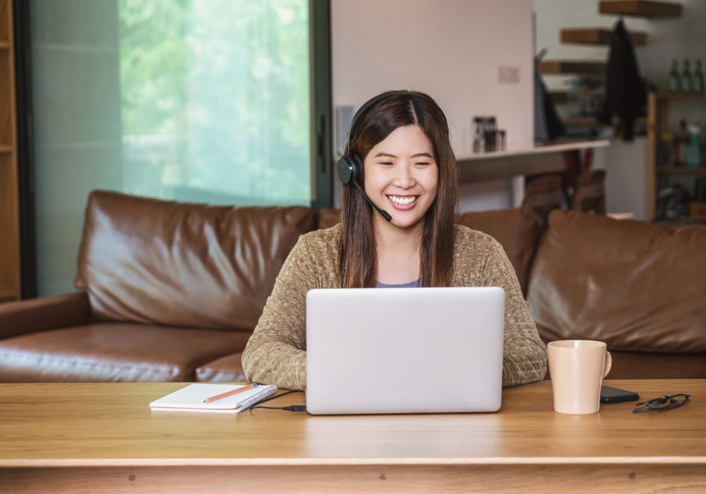 Asian business woman using technology laptop and headphone for working from home in indoor house by video conference call, startups and business owner, social distance and self responsibility